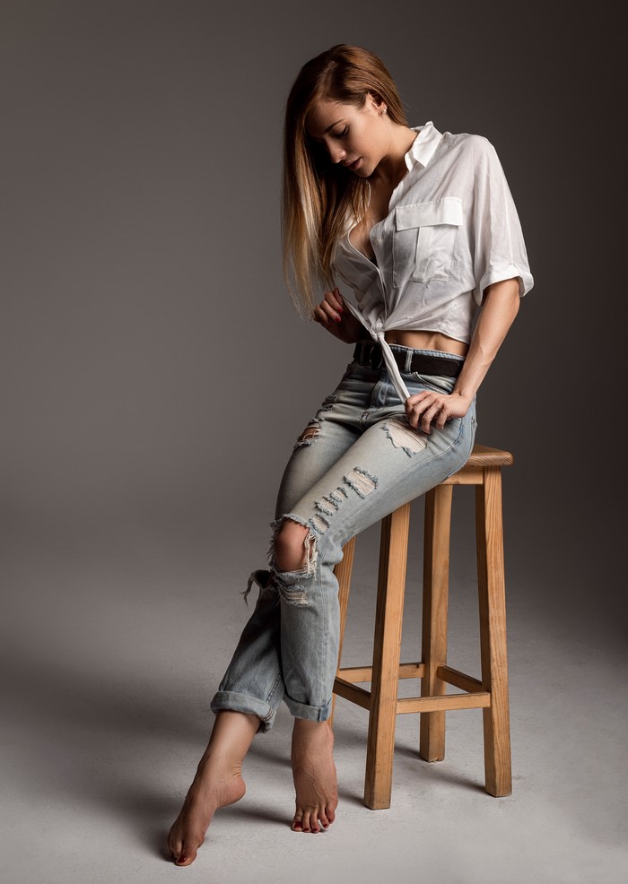 Woman in ripped jeans and white shirt sitting on stool