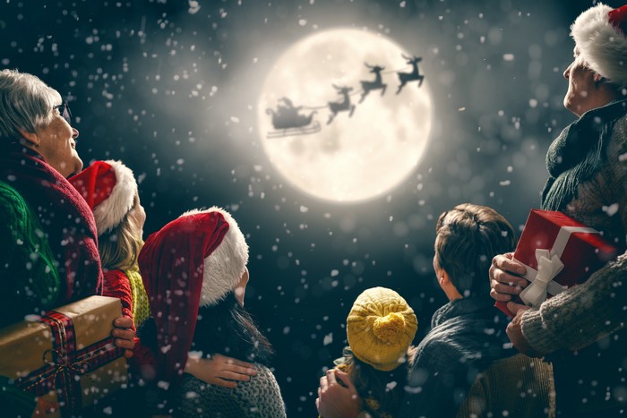 Family watching Santa Claus and reindeer in the moonlit sky
