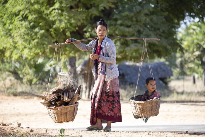 Asian woman carrying baskets with child and firewood