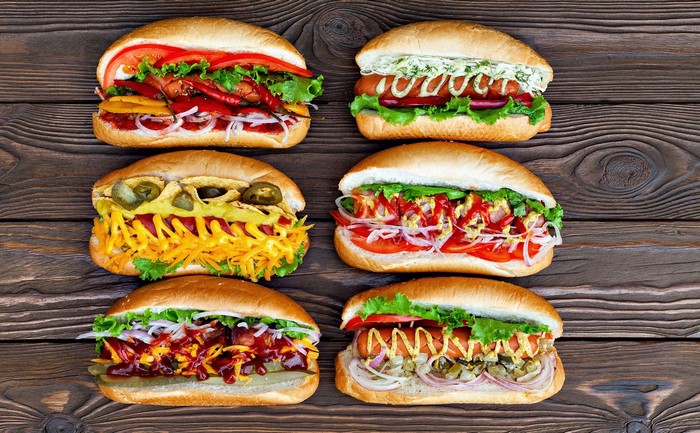 Six gourmet hot dogs with various toppings on a wooden table