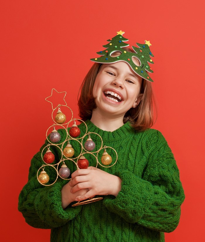 Girl in green sweater with Christmas tree mask and ornament holder