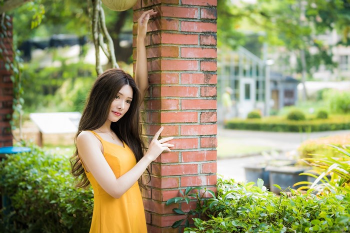 Asian woman in yellow dress posing by brick pillar