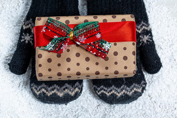Christmas gift wrapped in brown paper with polka dots held by mittens