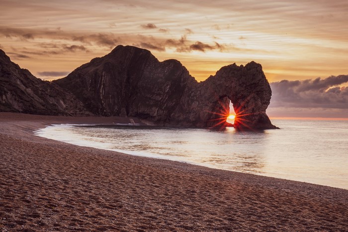 Sunrise through Durdle Door arch on a pebble beach