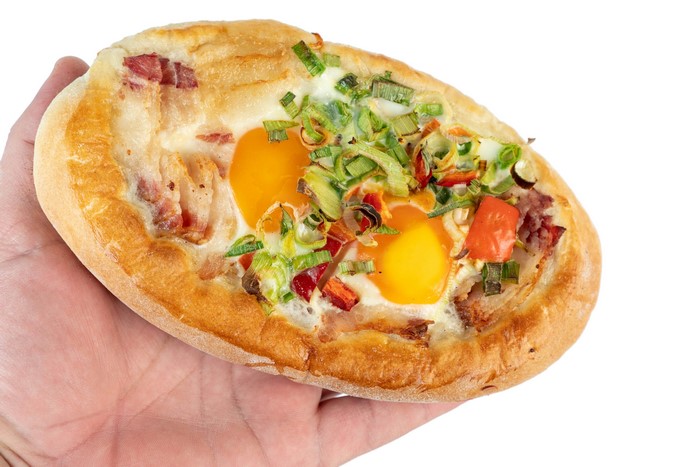 Khachapuri with eggs, bacon, and vegetables held in hand