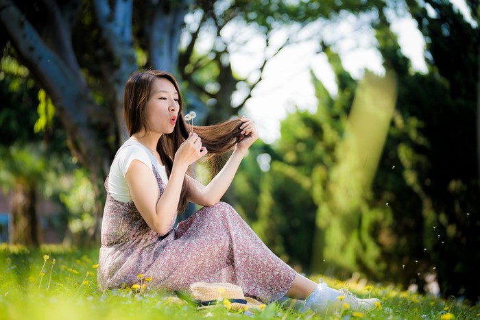 Asian woman blowing dandelions in a park