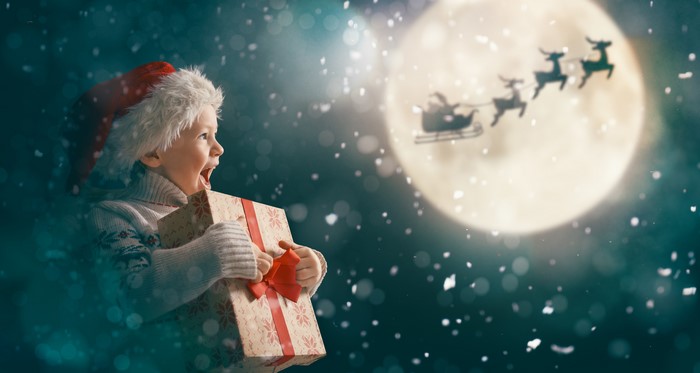 Child with Christmas gift watches Santa's sleigh in the moonlit sky