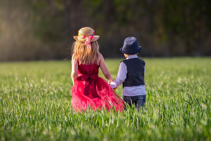 Two children holding hands in a grassy field
