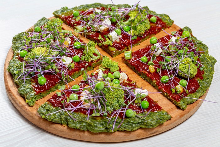 Green pizza with broccoli, peas, and microgreens on a cutting board
