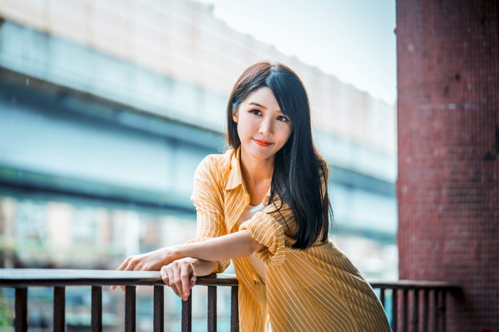 Asian woman in yellow shirt leaning on railing