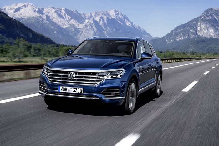 Blue Volkswagen Touareg driving on a highway with mountains