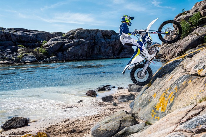 Husqvarna TE 300 motorcyclist performing a wheelie on rocky coast