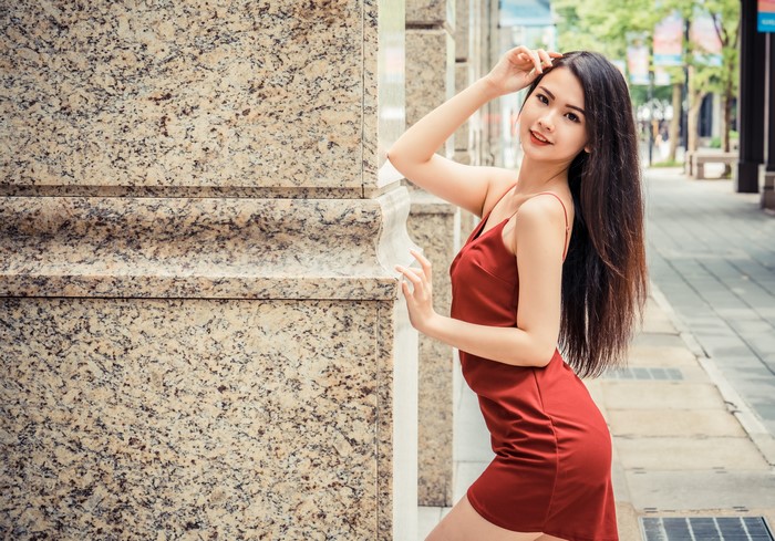 Asian woman in red dress posing by column