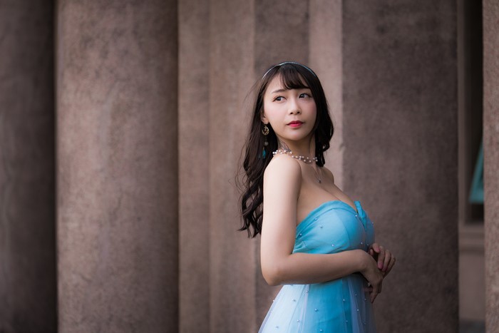 Asian woman in blue dress posing near columns
