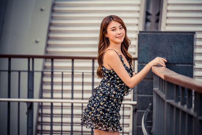 Asian woman in floral dress posing by railing