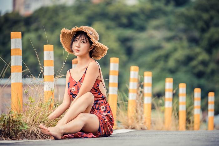 Asian woman wearing a hat and dress sitting on the road