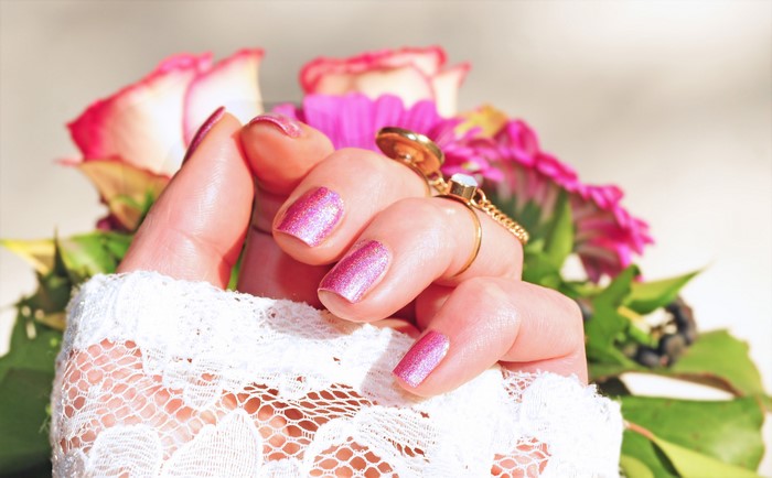 Hand with pink manicure and rings near roses