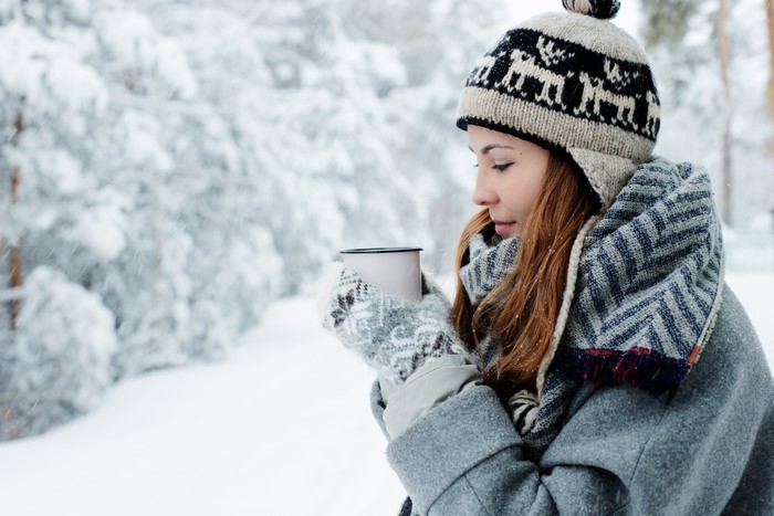 Woman in winter hat holding a mug in the snow