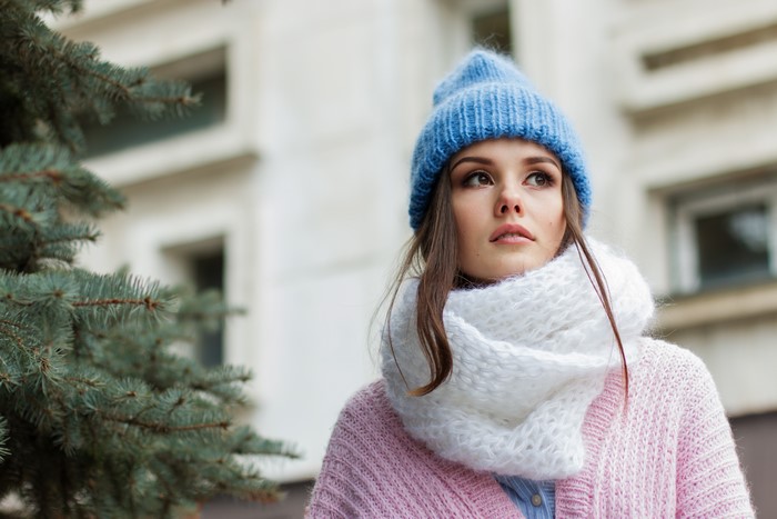 Brown haired girl wearing a blue winter hat and pink sweater