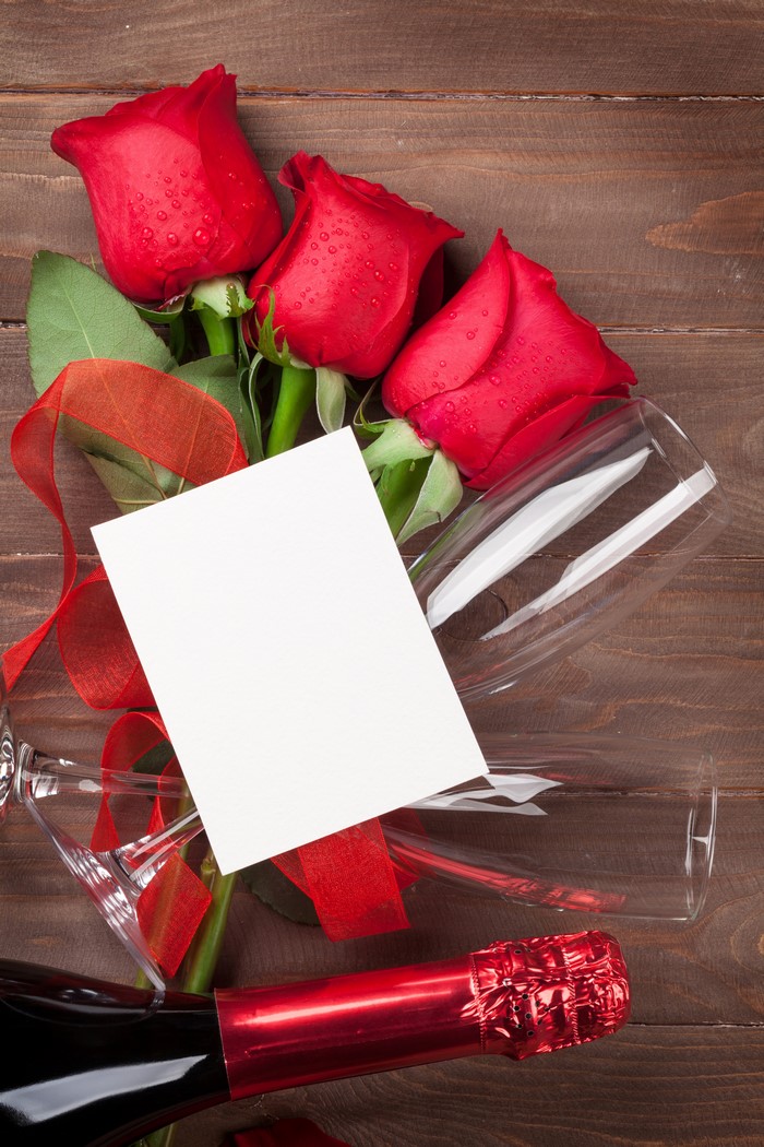 Red roses, champagne, and a blank card on wood