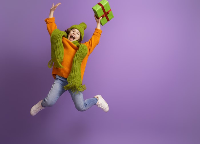 Girl in orange sweater jumping with gift