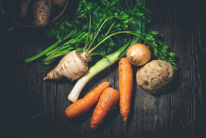 Vegetables including carrots, onion, parsnip, leek, and celeriac on wood planks