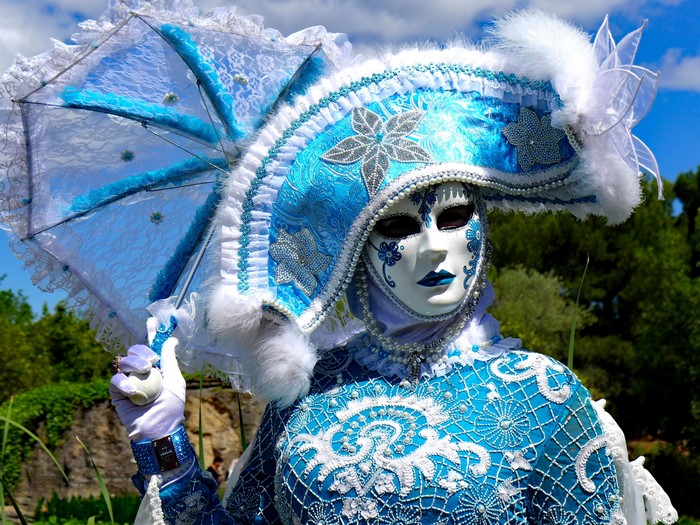 Person in blue and white Venetian costume with mask and umbrella