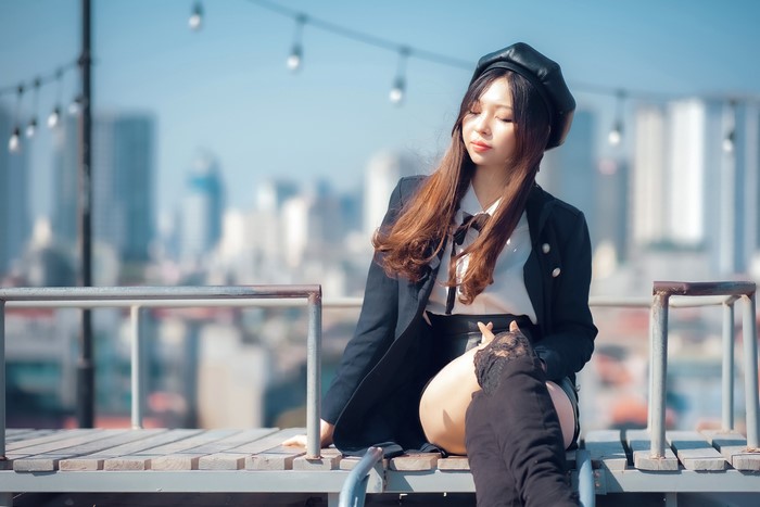 Asian woman wearing a beret and boots sitting on a rooftop