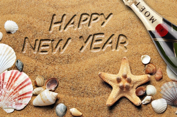 Happy New Year written in sand with seashells and champagne