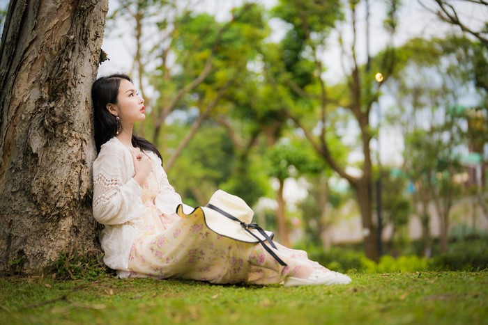 Asian woman sitting by a tree with a hat