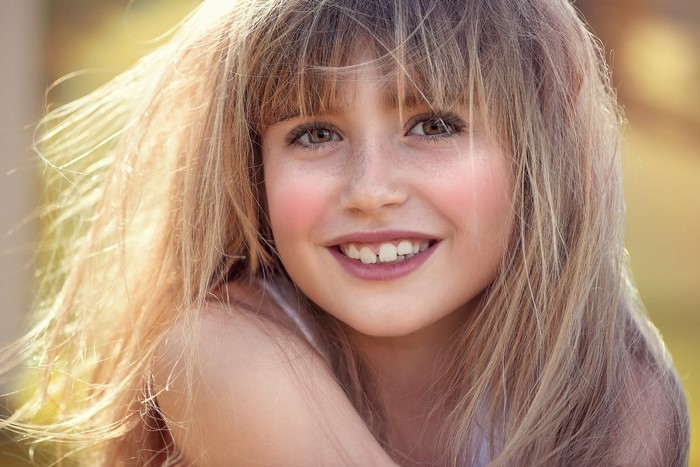 A young girl with blonde hair and freckles smiling