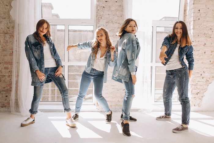 Four young women in denim outfits dancing