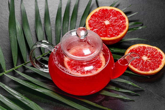 Glass teapot with grapefruit tea and palm leaves