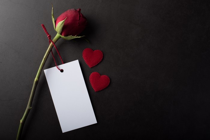 Red rose with tag and hearts on dark background