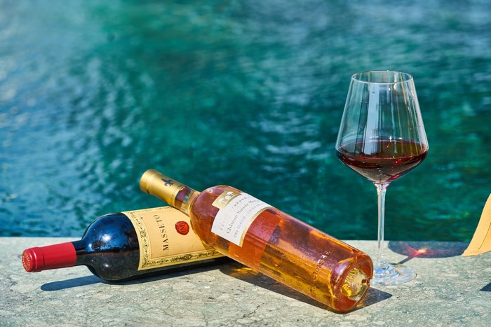 Two wine bottles and a glass of red wine by the pool
