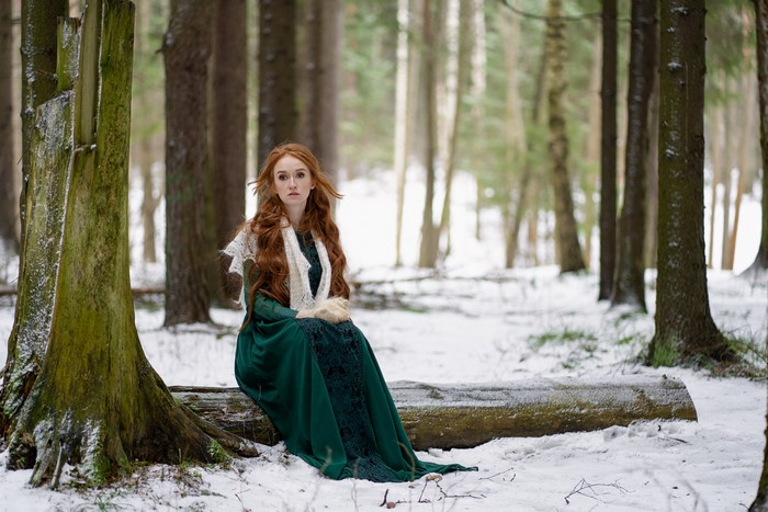 Redhead girl in green dress sitting in snowy forest