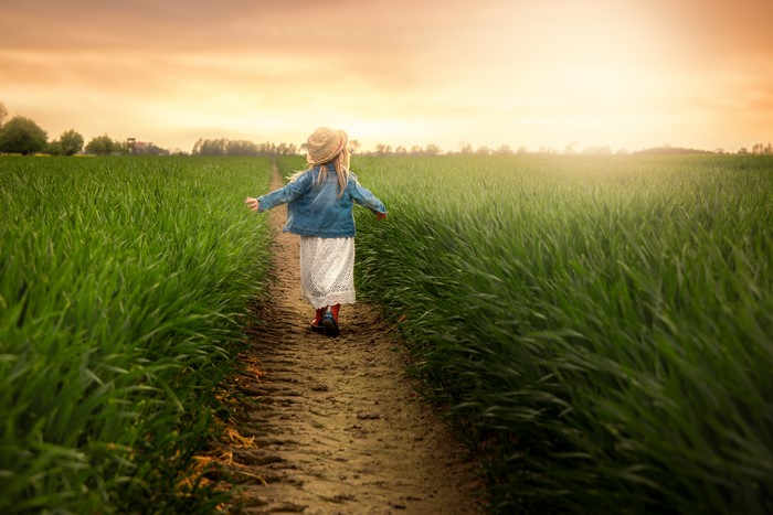 Girl in hat and jacket walking on a field trail