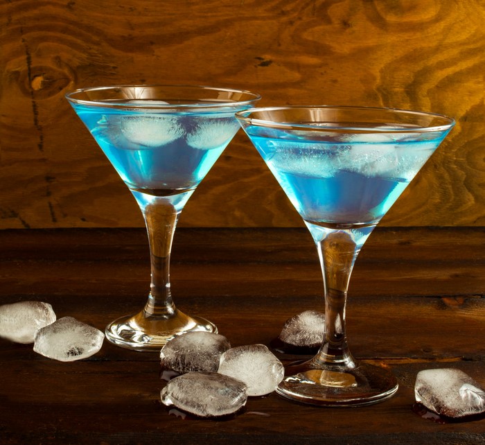 Two blue cocktails with ice on a wooden table