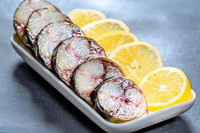 Sliced smoked fish with lemon slices on a platter