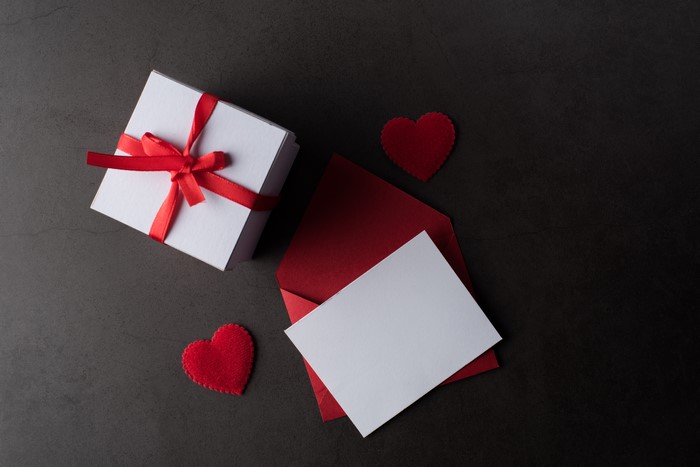 White gift box with red ribbon, red envelope, and white card on gray background