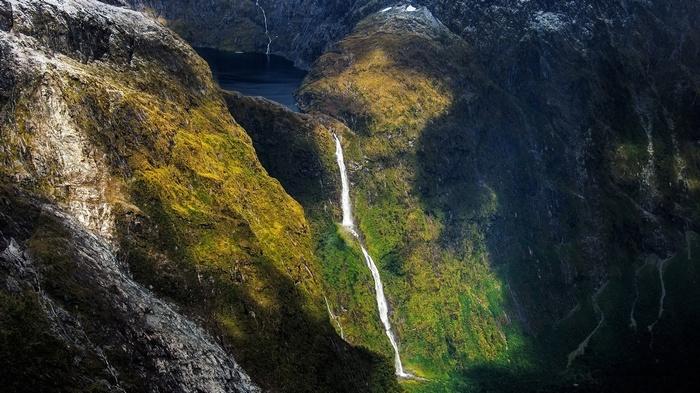 Waterfalls cascading down a moss-covered mountain into a dark lake