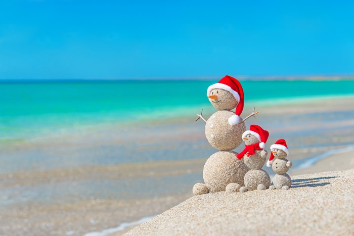 Sand snowmen with Santa hats on a beach