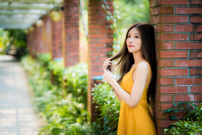 Asian woman in yellow dress leaning on brick pillar