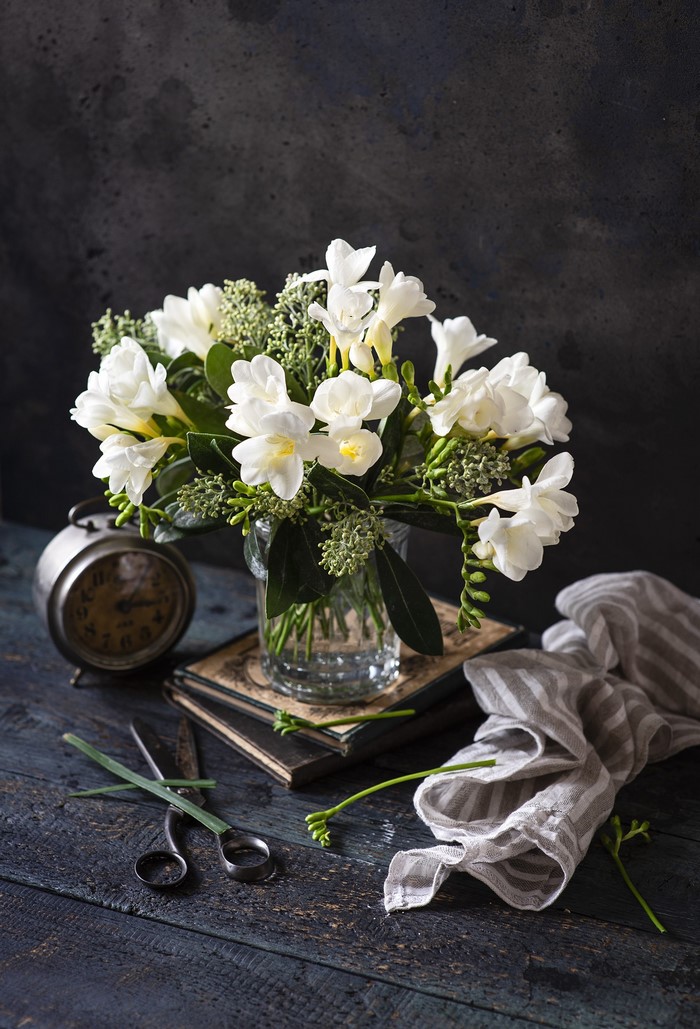 White Freesia flowers in a vase with a clock