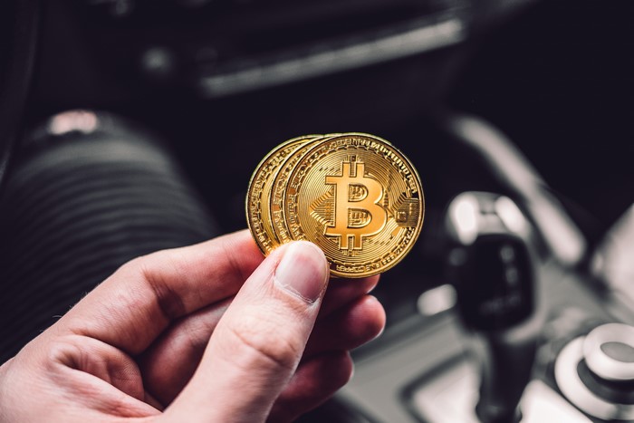 Hand holding Bitcoin coins in a car