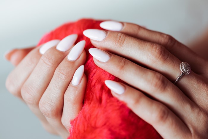 Hands with white manicure and ring holding red object