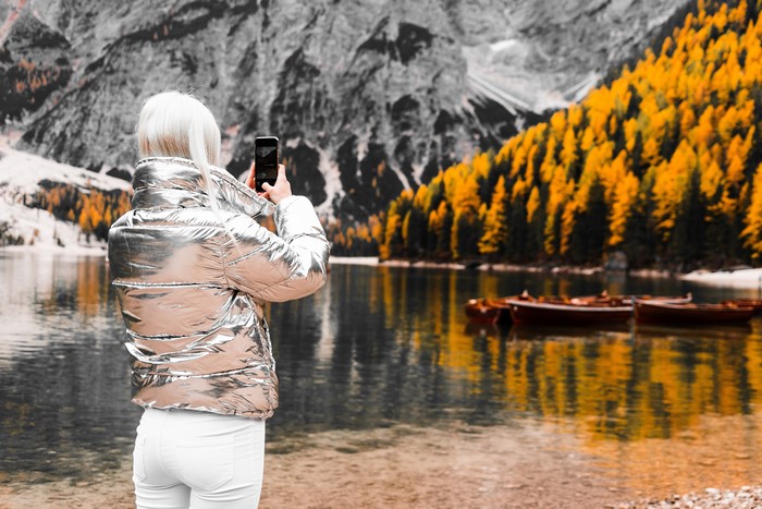Blonde girl taking photo with smartphone at lake