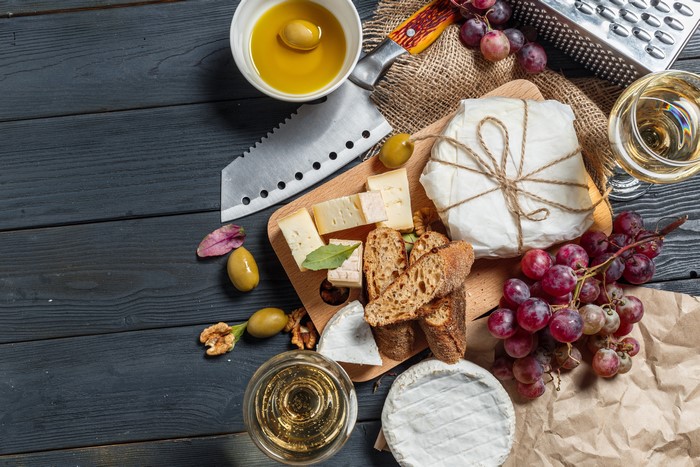 Cheese, Bread, Grapes, Wine, and Olives on a Cutting Board
