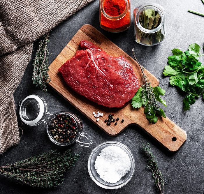 Raw steak with spices and herbs on a cutting board