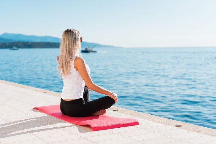 Woman meditating on a yoga mat by the sea